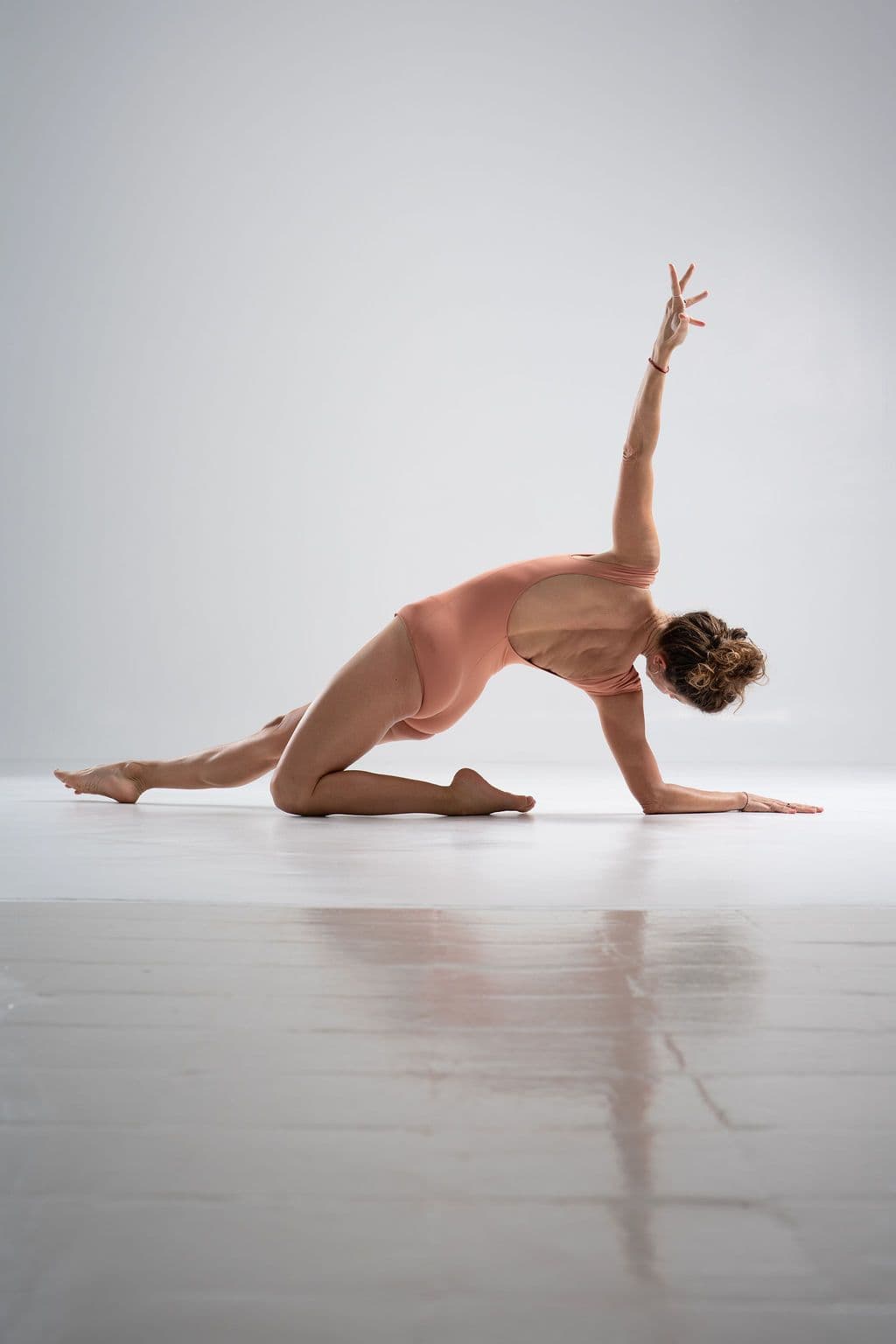 Lucia reaching upward from a grounded lunge in soft studio light